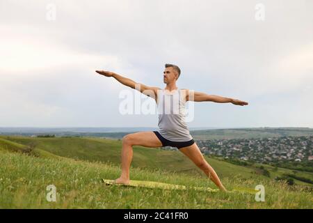 Mature man doing yoga exercise Valence on green grass in nature. Stock Photo
