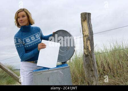 Elderly woman puts laptop in a garbage can Stock Photo