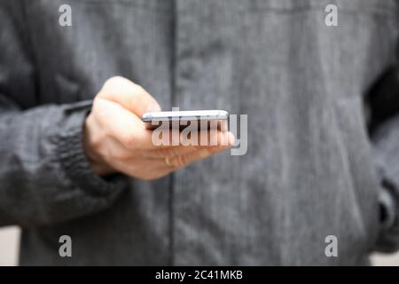 Closeup man in jacket holds smartphone his hands Stock Photo