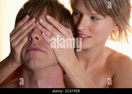 Young woman covers young man's eyes Stock Photo