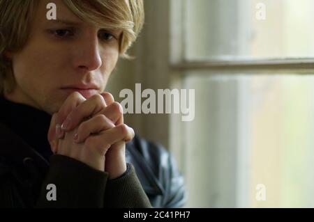 Thoughtful young man with praying hands Stock Photo
