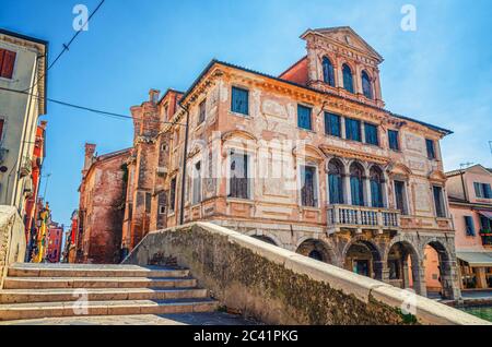 Stone brick bridge Ponte Caneva across Vena water canal and old building in historical centre of Chioggia town, blue sky background in summer day, Veneto Region, Northern Italy Stock Photo