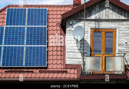 Solar panels on the roof of old wooden house with attic and small balcony Stock Photo