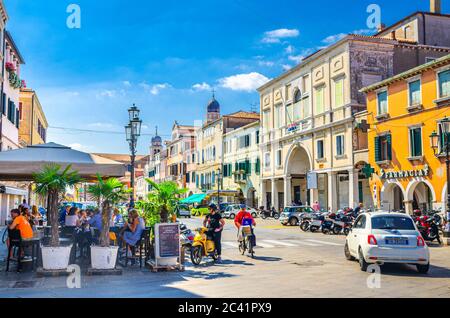 Chioggia, Italy, September 16, 2019: people in street restaurant , riding cars, colorful multicolored buildings in historical town centre, blue sky background in summer day, Veneto Region Stock Photo