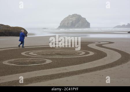 A woman walking a Circles in the Sand labyrinth at Face Rock Beach in Bandon, Oregon, USA. Stock Photo