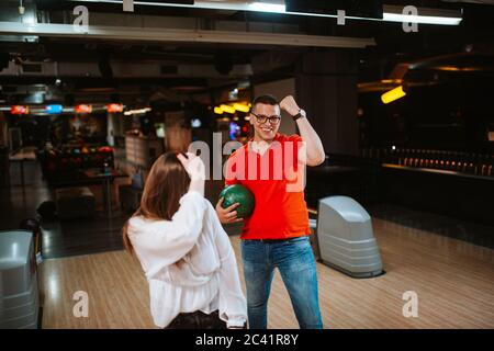 A caucasian man and woman with balls in their hands are playing bowling and making grimaces. Love at the bowling club Stock Photo