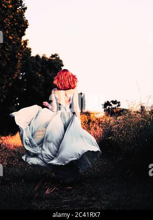 Beautiful redhead wearing elegant flowy dress in a meadow Stock Photo