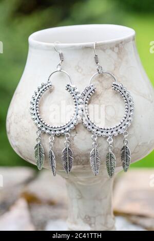 Silver metal earrings in the shape of dream catcher on white cup, green background Stock Photo