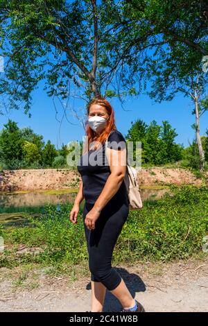 Middle-aged red-haired woman walking on a path surrounded by nature with masks to protect themselves from the coronavirus. Healthy life concept Stock Photo