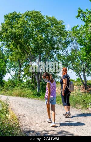 Middle-aged red-haired woman with her young daughter walking on a path surrounded by nature with masks to protect themselves from the coronavirus. Hea Stock Photo