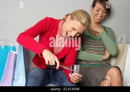 Young blonde woman next to a brunette woman cuts a credit card - shopping frenzy - bankruptcy Stock Photo