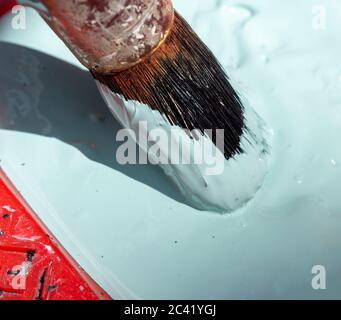 Old and rusty paint brush laying in a paint tray with pastel green paint. Stock Photo