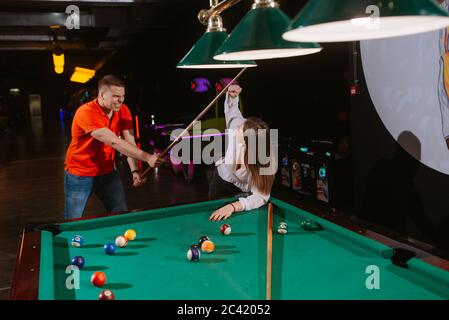 A beautiful young caucasian woman and a caucasian man are hitting each other with billiard cues. Love and fun Stock Photo