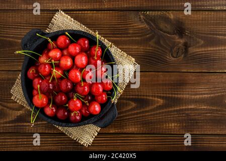 Sweet red cherries in a black bowl on a dark brown wooden table with copy space for text. Top view. Stock Photo