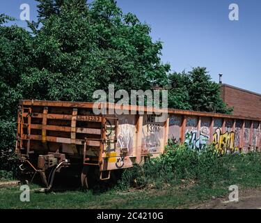 Abandoned MBTA train car covered in graffiti sits on service tracks in Wakefield, MA. Overgrown grass and trees surround the car with bright blue sky Stock Photo