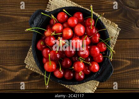 Sweet red cherries in a black bowl on a dark brown wooden table. Top view. Stock Photo