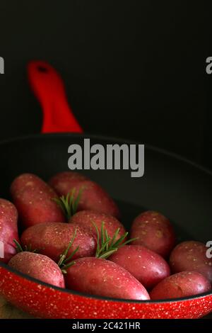 Vegetables food concept. Red potatoes and rosemary inside a pan on wooden table. Stock Photo