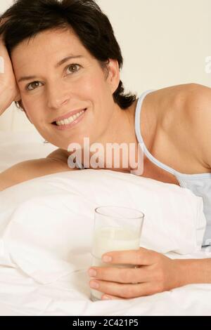 Elderly woman lying in bed, holding a glass of milk in her hand Stock Photo