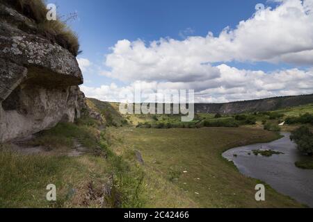 Crag is overhanging above the river. The beautiful landscape. There are a valley of the river and the blue sky with clouds. Stock Photo