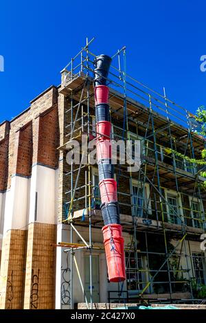 Red and black construction trash chute used during a house renovation, scaffolding on house facade Stock Photo