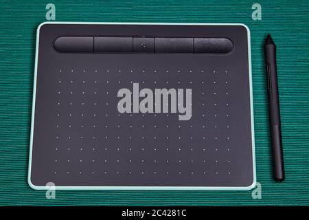 An electronic input device for a personal computer, a graphic tablet with a stylus pen, lies on a table covered with a green cloth. Drawing board for Stock Photo