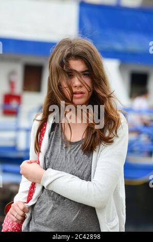 Portrait of teenage brunette girl wearing a jeans, with red backpack in a windy day, ready to board the ship