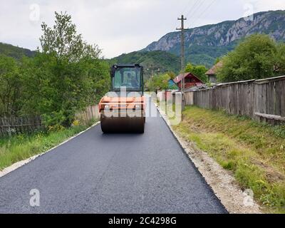 Asphalt pneumatic compactor roller on newly built village road in Salciua village, Apuseni, Transylvania, Romania. Road construction procedure of vibr Stock Photo