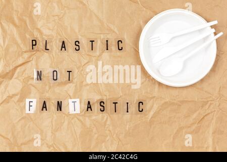 Disposable appliances plate, fork, spoon, knife, phrase from letters on transparent base Plastic not fantastic on brown crumpled craft paper. Eco, zer Stock Photo
