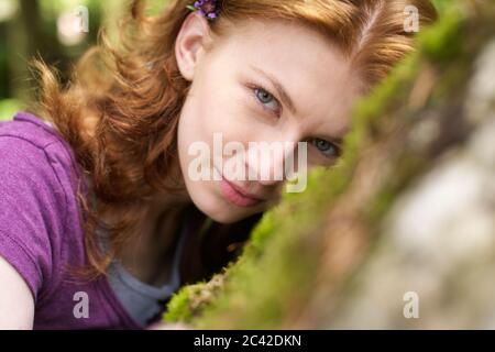 Young woman leans against moss-covered rock and looks at the camera Stock Photo