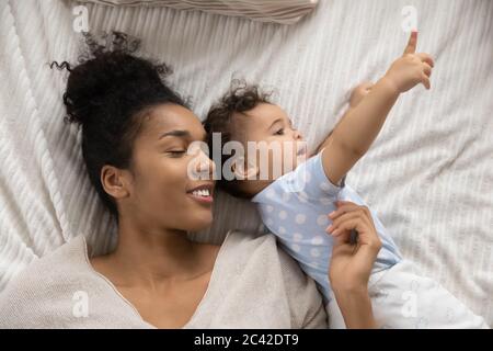 Smiling sleepy African American mother and toddler lying in bed Stock Photo