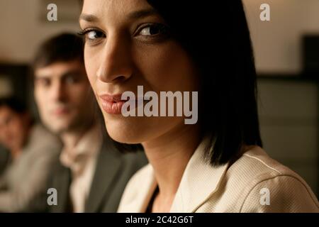 Elegant woman with dark hair sits in a row with two men - eatery - bar Stock Photo