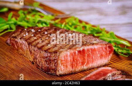 Sliced grilled rare beef steak served with arugula on wooden board. Stock Photo