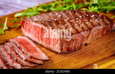 Delicious and healthy grilled medium rare beef steak on wooden board with arugula. Stock Photo