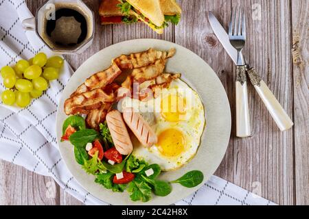 Tasty breakfast with eggs, sausages, bacon, toast and cup of coffee. Stock Photo