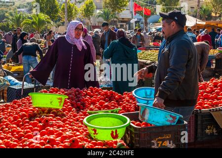 Green and blue plastic bowls stand ready to hold weighed-out tomatoes at the weekly market in Sefrou, Morocco, a Moroccan flag flies in the background. Stock Photo