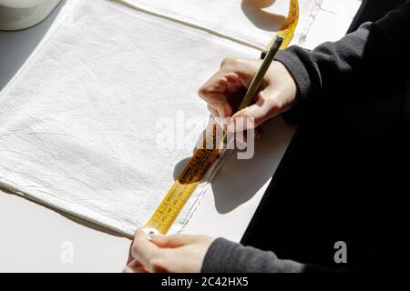 Side angle view of tailor working at table with sewing machine and marking piece of cloth with pencil while using measuring tape Stock Photo