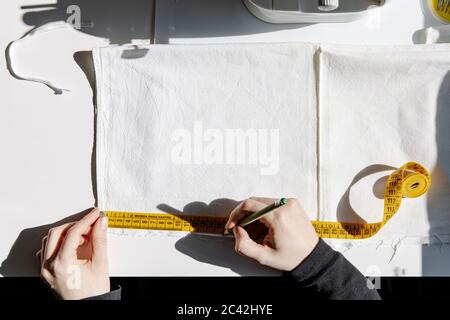 Top view of tailor working at table with sewing machine and marking piece of cloth with pencil while using measuring tape Stock Photo