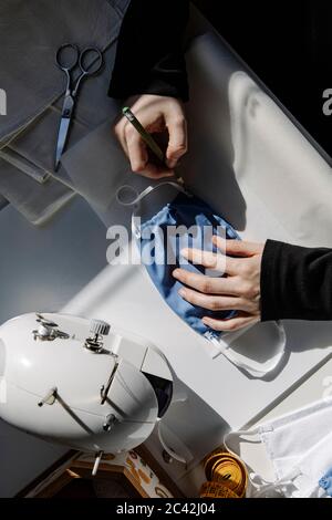 Top view of crop craftswoman taking measures on paper with homemade fabric mask in workshop Stock Photo