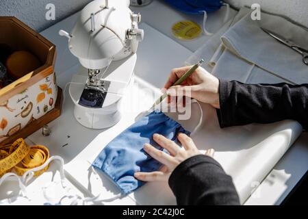 Top view of crop craftswoman taking measures on paper with homemade fabric mask in workshop Stock Photo