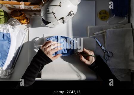 Top view of crop craftswoman taking measures on paper with homemade fabric mask in workshop Stock Photo