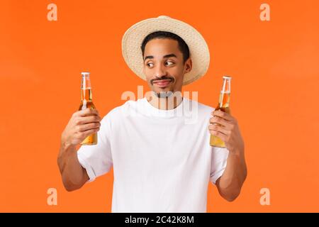 Happy, smiling and cheerful caucasian guy in hat relaxing during travelling tropical country, cooling himself with cold tasty drink, holding two Stock Photo