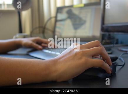 Closeup on the hand of a woman using her computer, with a keyboard, laptop and monitor on the background Stock Photo
