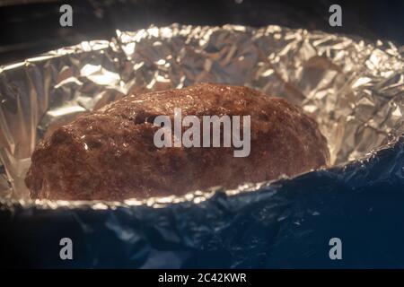 Grounded beef rolled with ham and cheese inside, on a foil tray inside the oven Stock Photo