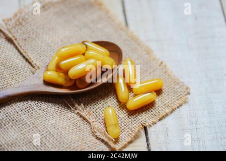 Yellow capsule medicine or supplementary food from nature for health / Royal jelly capsules in wooden spoon and sack background Stock Photo