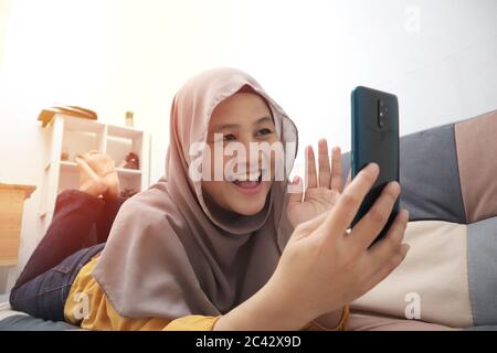 Closeup of Asian muslim woman using a smart phone. Happy smiling gesture having good news when communicating on internet online, video call, selective Stock Photo