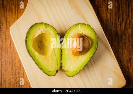 An avocado cut into half on a wooden cutting board with a dark background Stock Photo