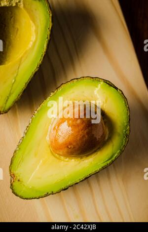 An avocado cut into half on a wooden cutting board with a dark background Stock Photo