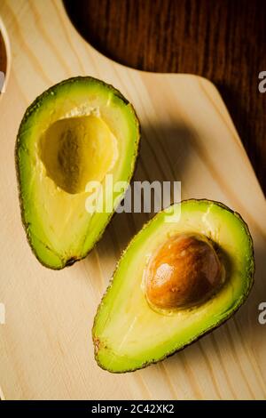 An avocado cut into half on a wooden cutting board with a dark background Stock Photo