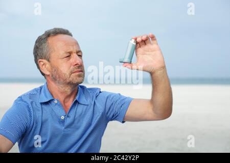 Middle-aged man using an inhaler on the beach Stock Photo