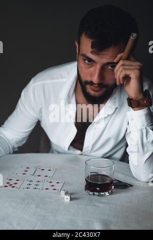 Portrait of an experienced gambler. Gambler young man drinking cigar and whiskey. Stock Photo